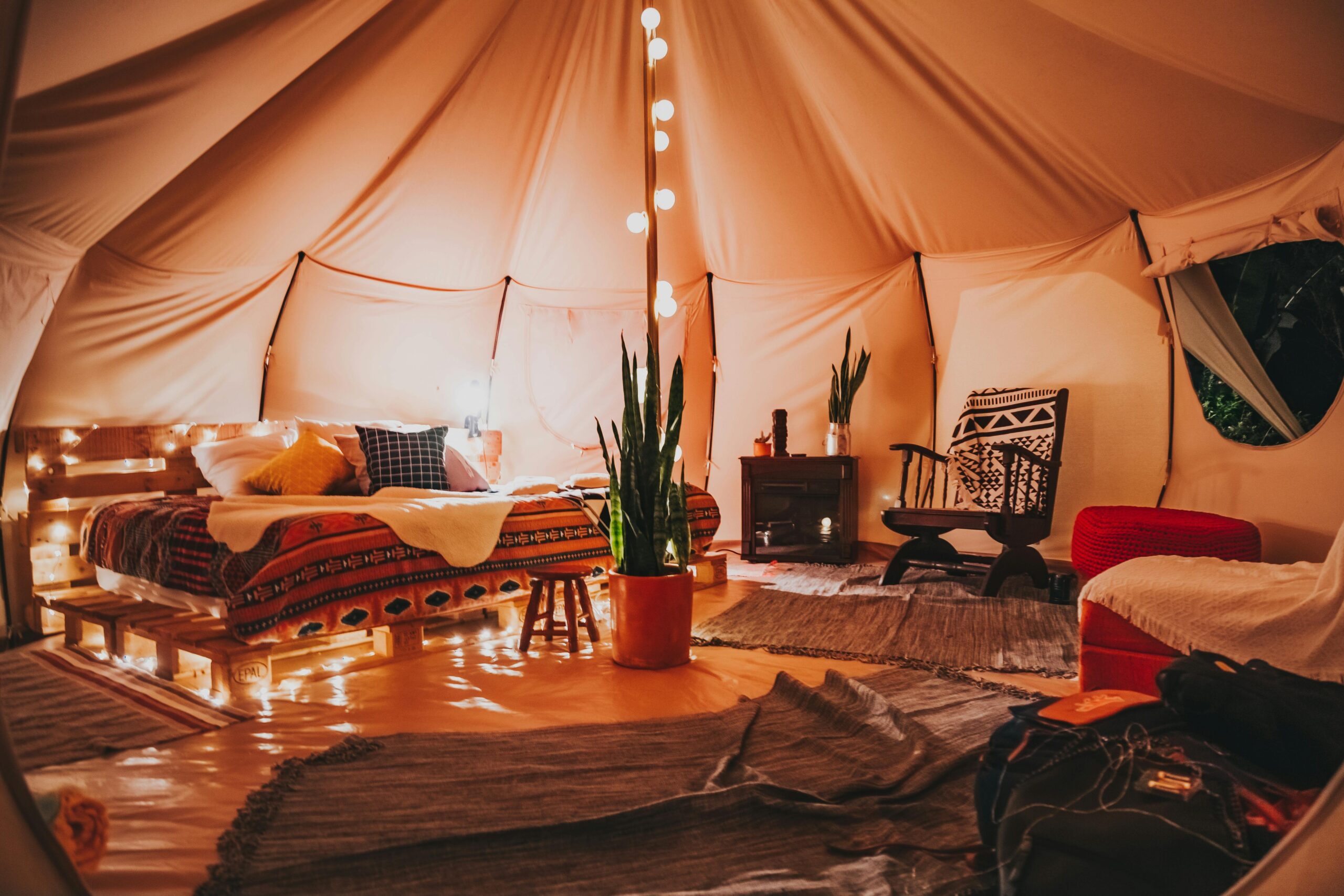 Luxurious and cozy glamping tent interior with soft lighting, stylish decor, and plants, perfect for relaxation.